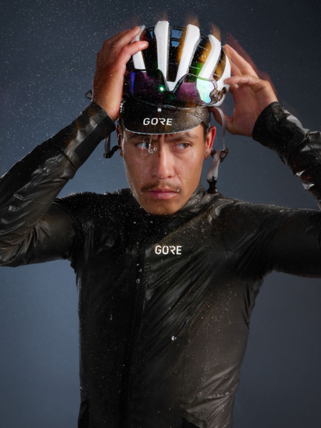 A glowy and slightly motion-blurred image of a road rider in wet weather riding apparel standing and adjusting their helmet in the rain. 